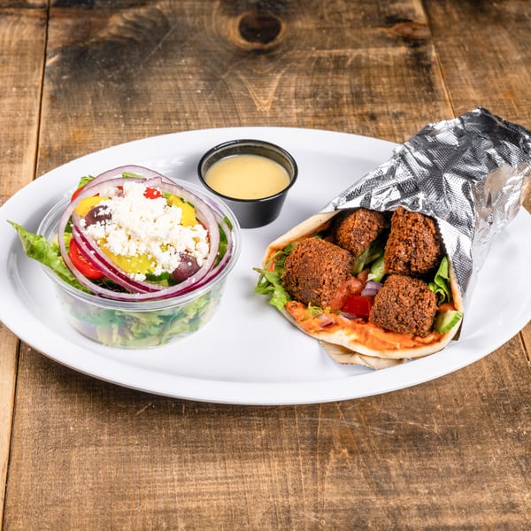 Falafel wrap with a side salad topped with feta cheese and a small cup of dressing.