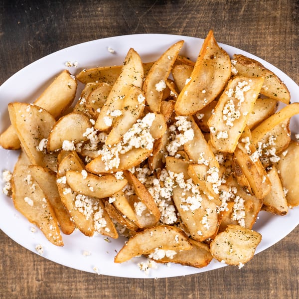 Golden potato wedges topped with crumbled feta cheese and herbs on a white platter.