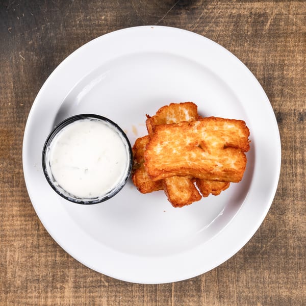 Golden-brown fried cheese curds with a side of white dipping sauce on a white plate.