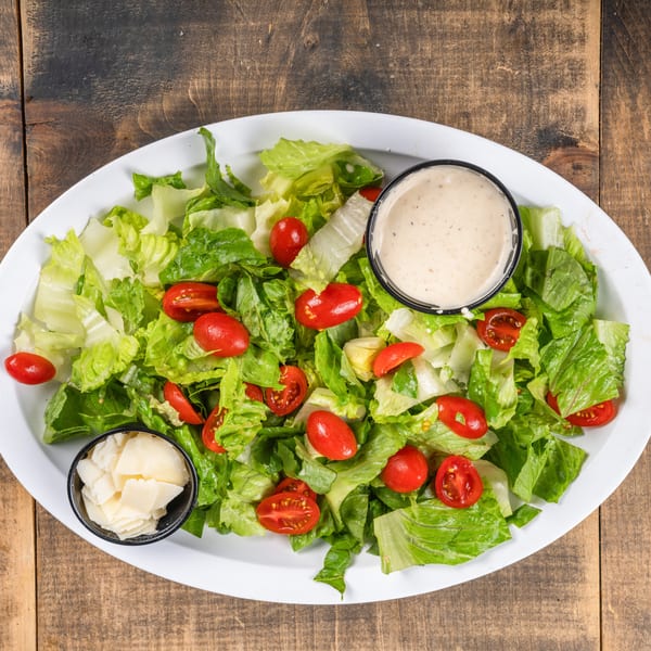 Fresh green salad with cherry tomatoes, dressing, and shaved cheese on a white platter.