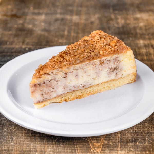 Slice of cheesecake with a crumbly nut topping on a white plate, on a rustic wooden table.