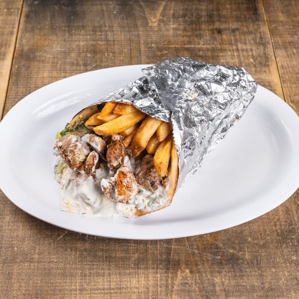 A shawarma wrap with meat, fries, and white sauce, partially wrapped in foil on a white plate.