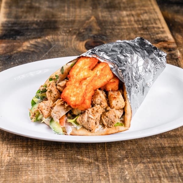 Chicken and halloumi wrap, partially wrapped in foil, on a white plate on a wooden table.