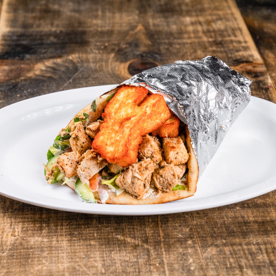 Chicken and halloumi wrap, partially wrapped in foil, on a white plate on a wooden table.
