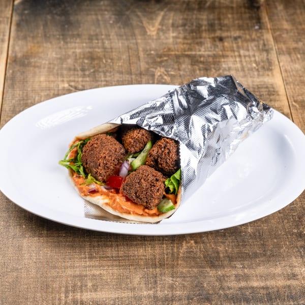 Falafel wrap with lettuce, tomatoes, onions, and sauce, partially wrapped in foil on a white plate.